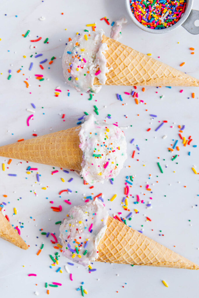 Cake batter ice cream in cones with sprinkles everywhere.