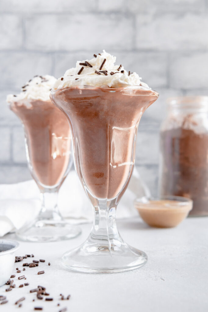 Two milkshake glasses filled with a chocolate milkshake and whipped cream.