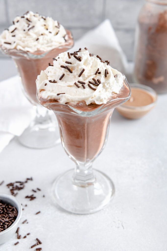 A chocolate milkshake with dairy-free almond whipped cream and chocolate sprinkles.