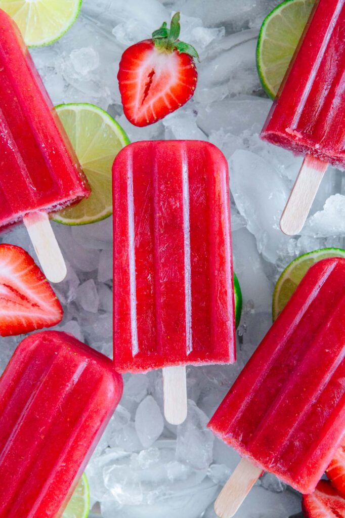 Popsicles surrounded by lime slices and strawberries.