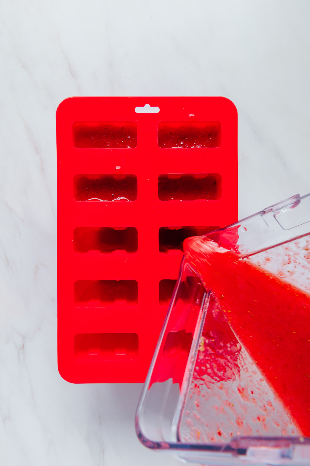 Strawberry lime mixture being poured in a popsicle mold.