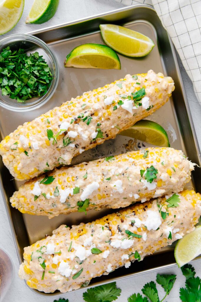 Elote with feta, cilantro, and lime wedges.