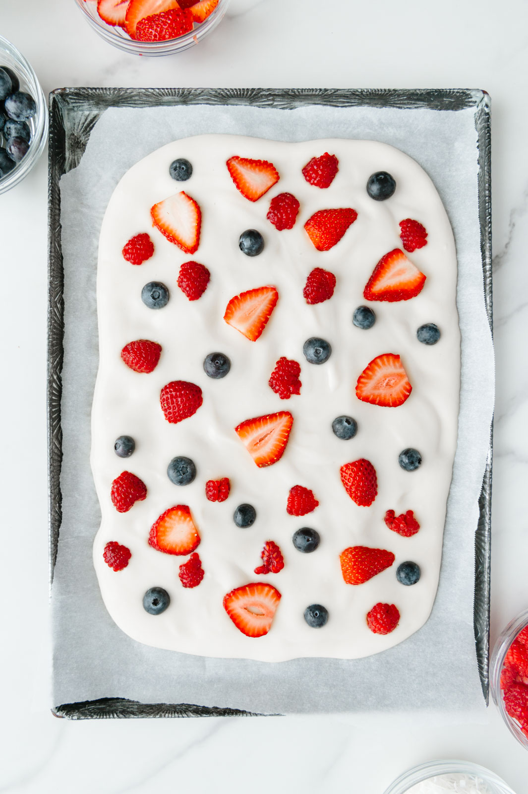 Raspberries added to dairy-free yogurt spread out on a baking sheet.