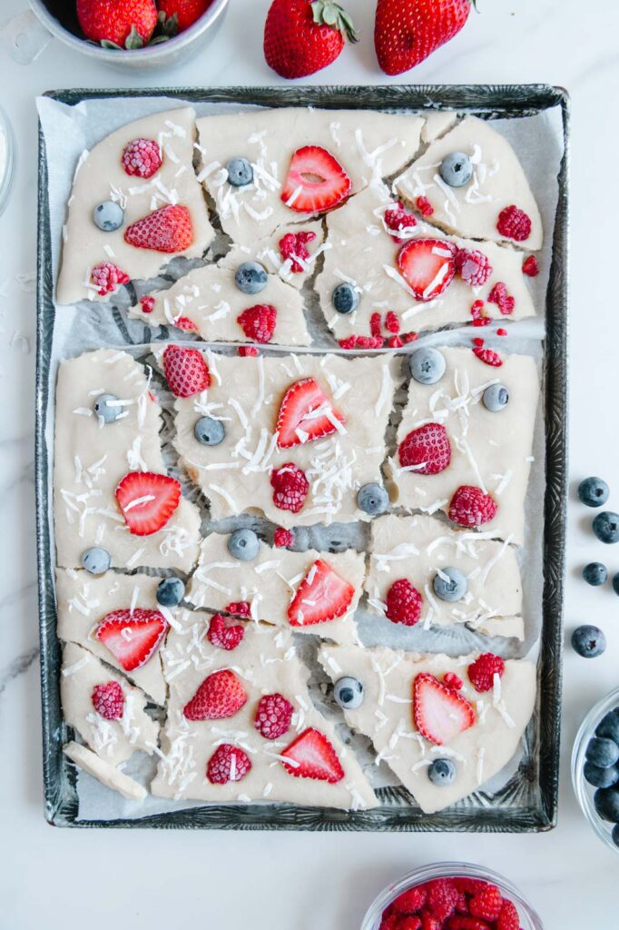 Frozen yogurt bark with fresh berries and shredded coconut on a baking sheet.