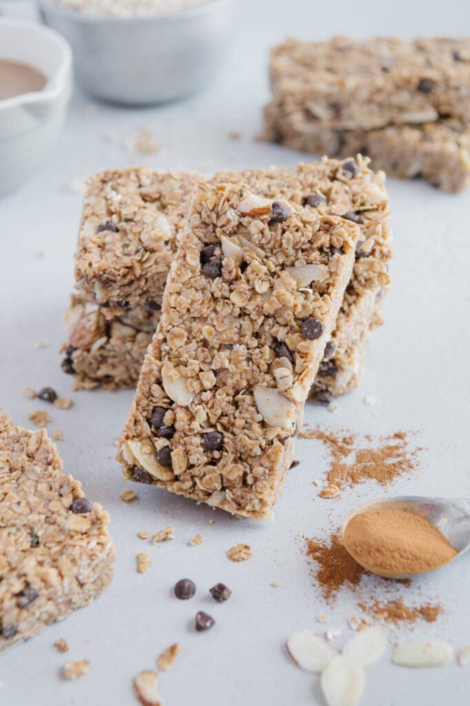 A granola bar with hemp seeds. almonds, and chocolate chips leaning on a stack of granola bars.
