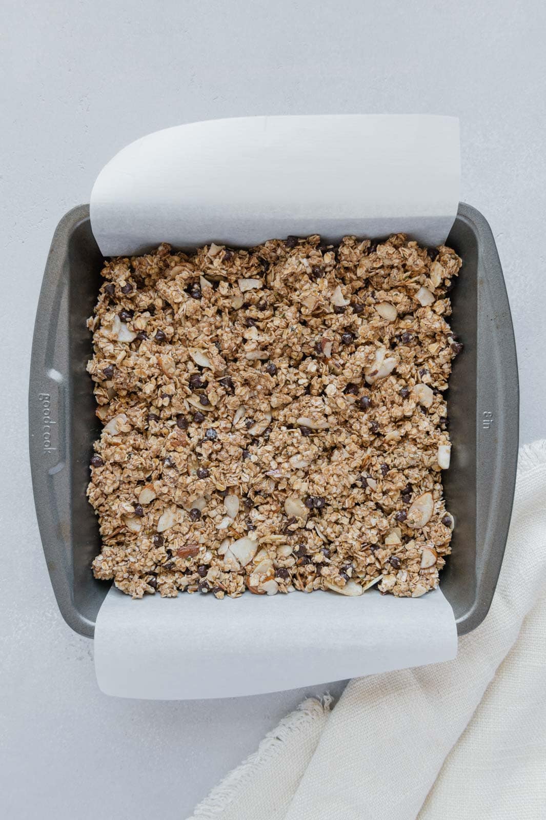 Granola bar mixture in an 8x8 baking pan lined with parchment paper.