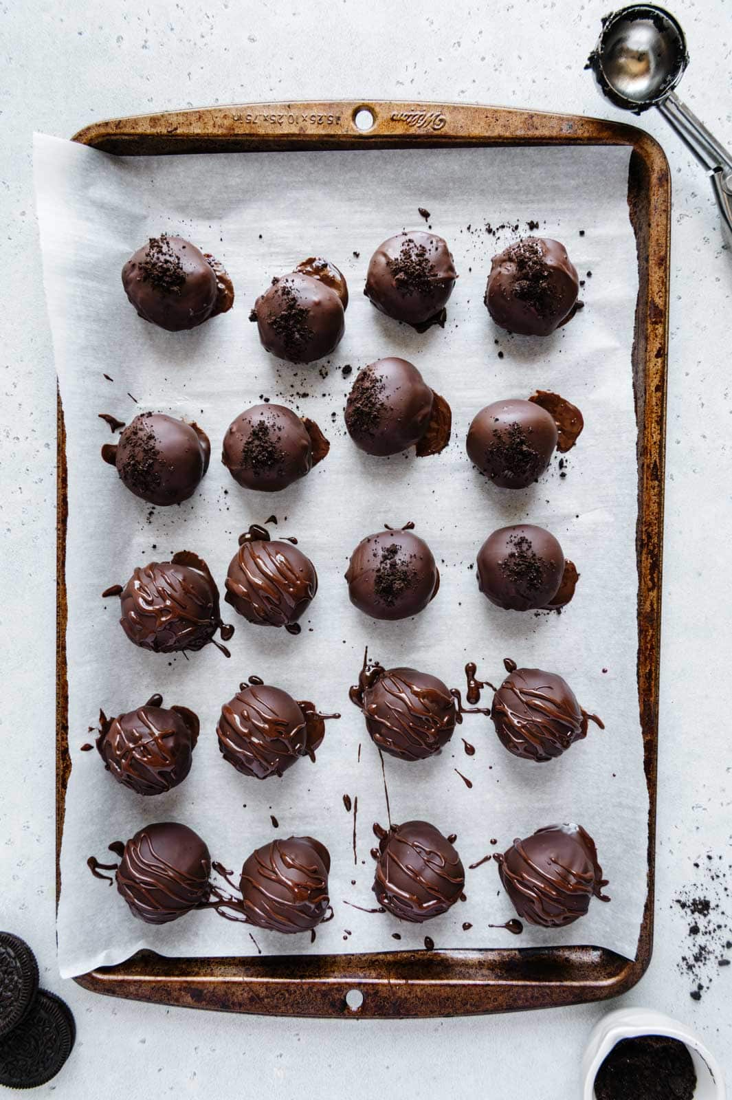Oreo truffles drizzled with chocolate and crushed Oreos on a baking tray.