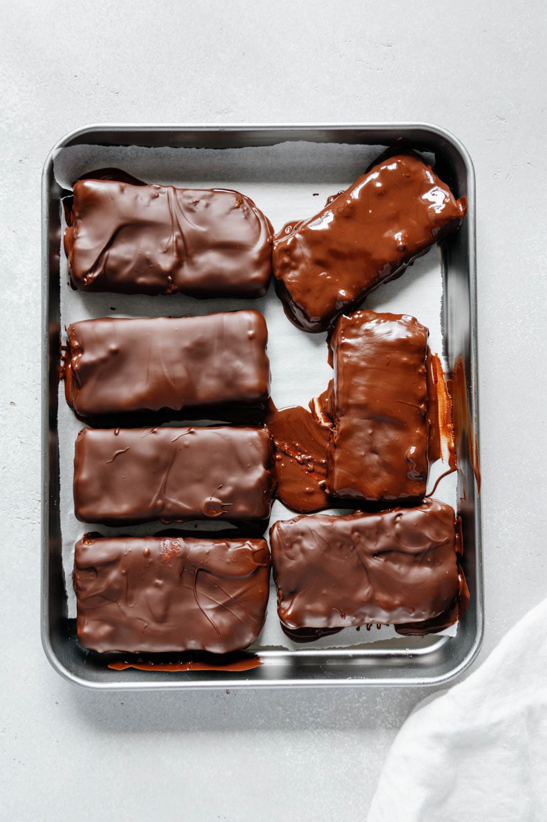 Butterfingers bars dipped in chocolate on a baking sheet ready to set.