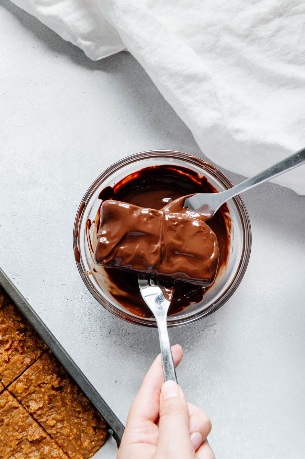 Two forks dipping a Butterfingers bar in melted chocolate.