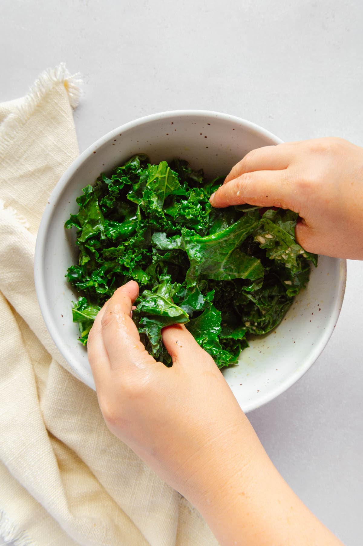 Hands massaging the salad dressing into curly kale.