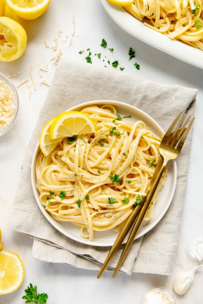A plate of pasta al limone with gold silverware.