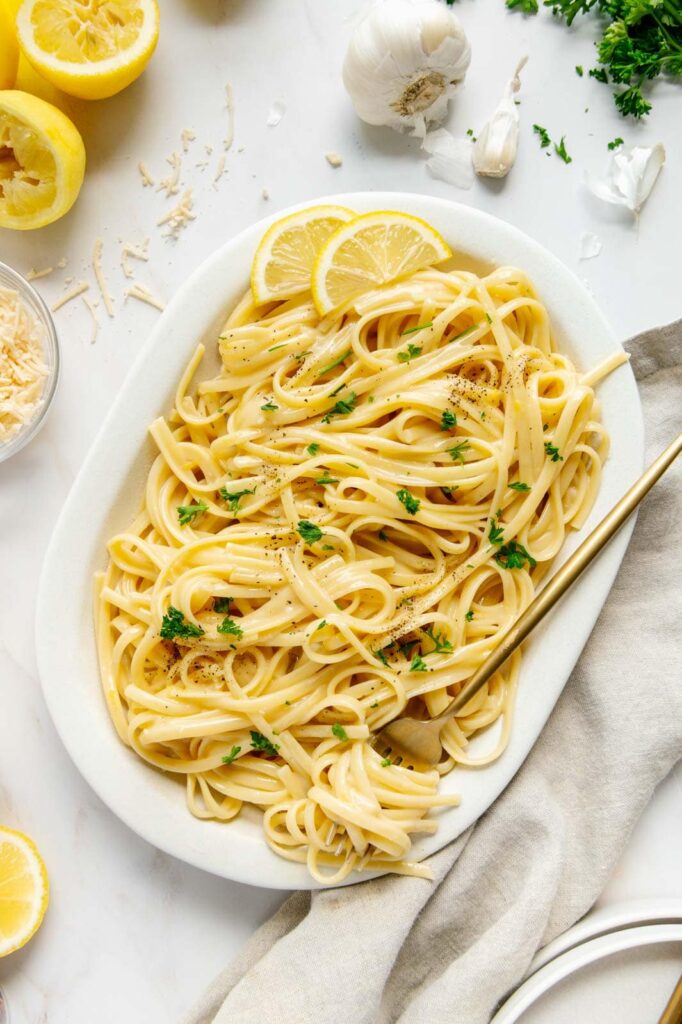 A serving platter of pasta al limone with fresh parsley and cracked black pepper.
