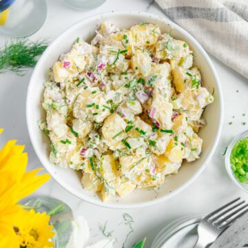 A serving bowl with vegan potato salad garnished with dill and chives.