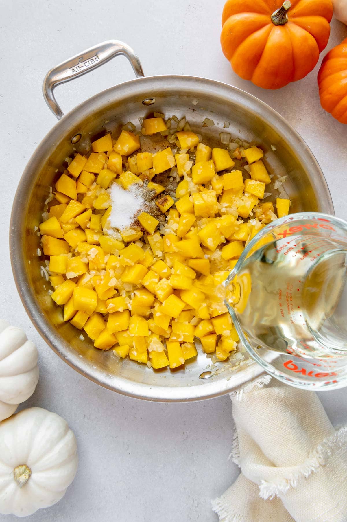Pumpkin cubes, onions, salt, pepper, and nutmeg in a saucepan with white wine being poured over it.
