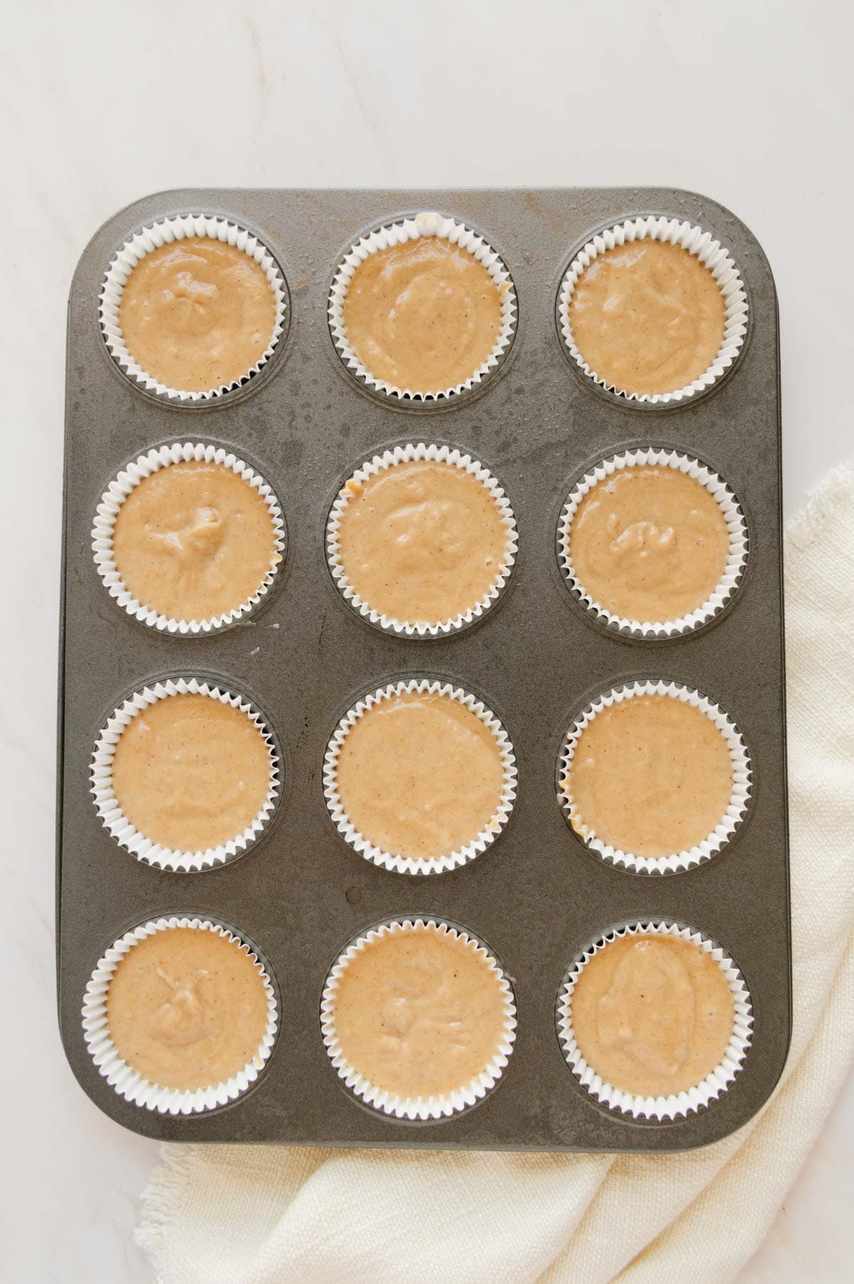 Chai muffin batter in a muffin tin lined with white muffin liners.