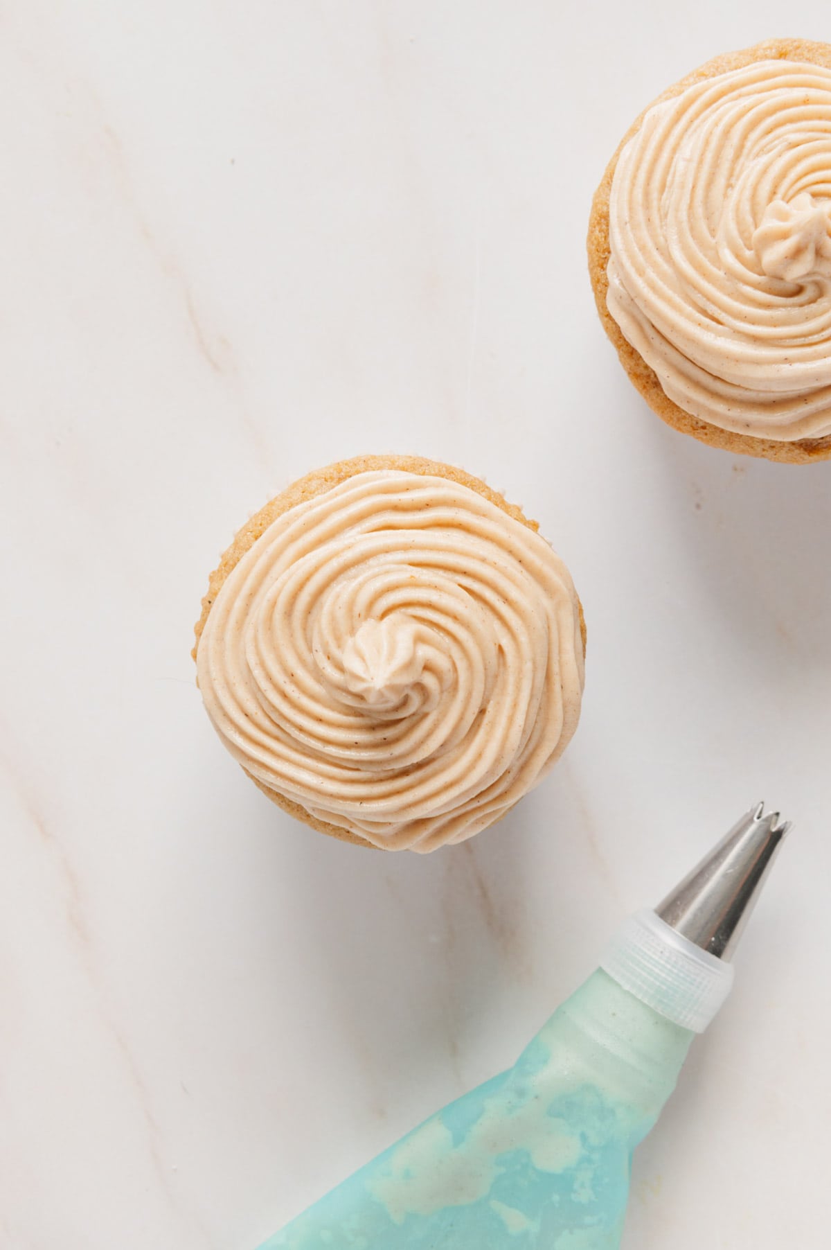 A chai cupcake being frosted with vegan chai buttercream frosting.