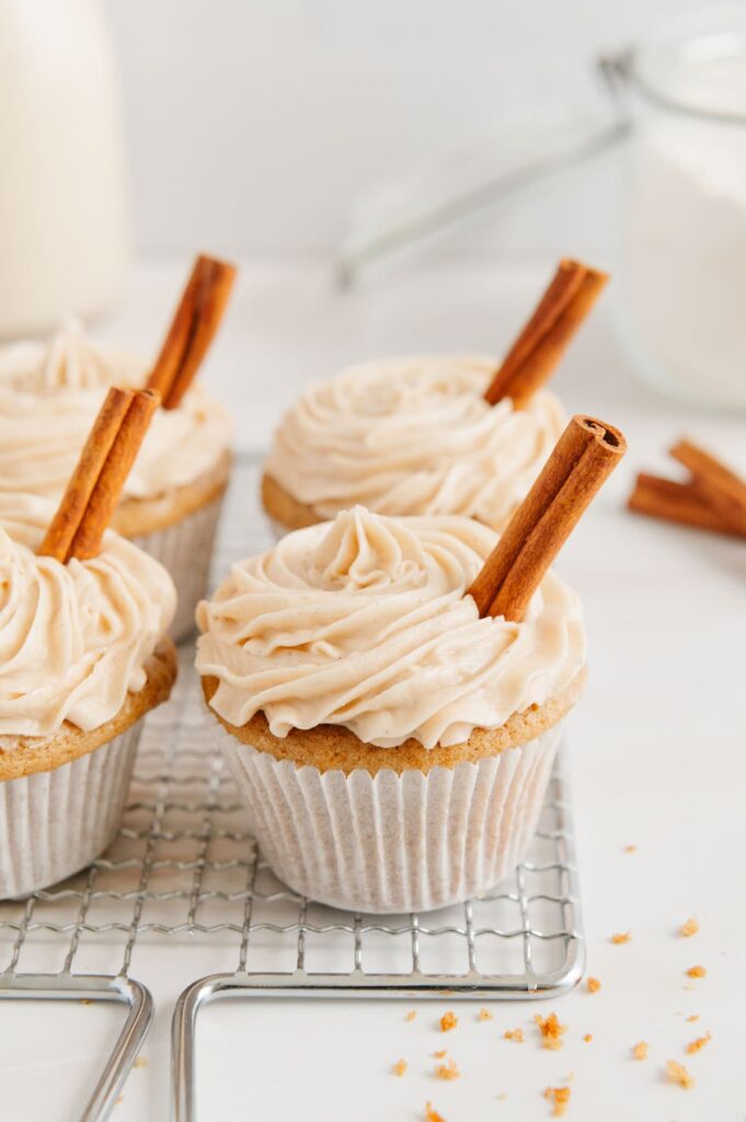 Chai cupcakes on a cooling rack frosted and garnished with cinnamon sticks.