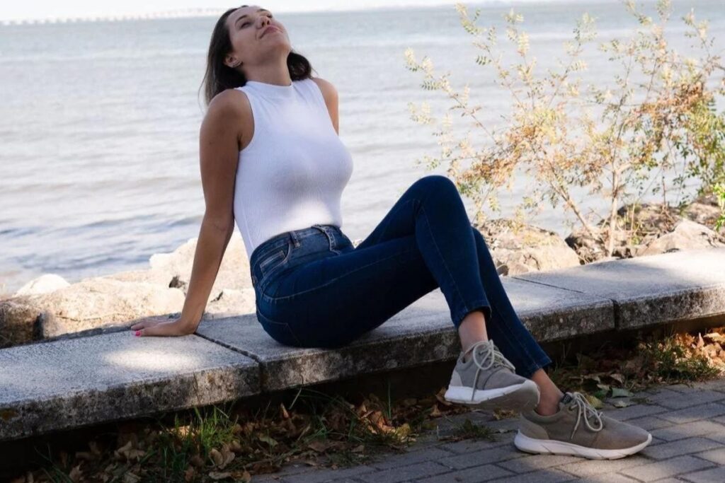 A woman sitting by a river in her 8000 Kicks shoes.