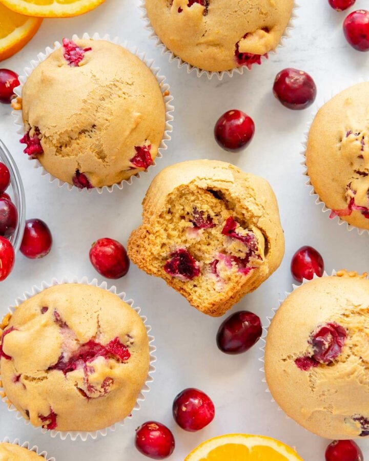 Scattered muffins and cranberries with a muffin in the center with a bite taken out of it.