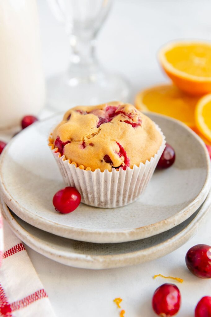 A cranberry orange muffin on a plate with fresh cranberries and orange zest.