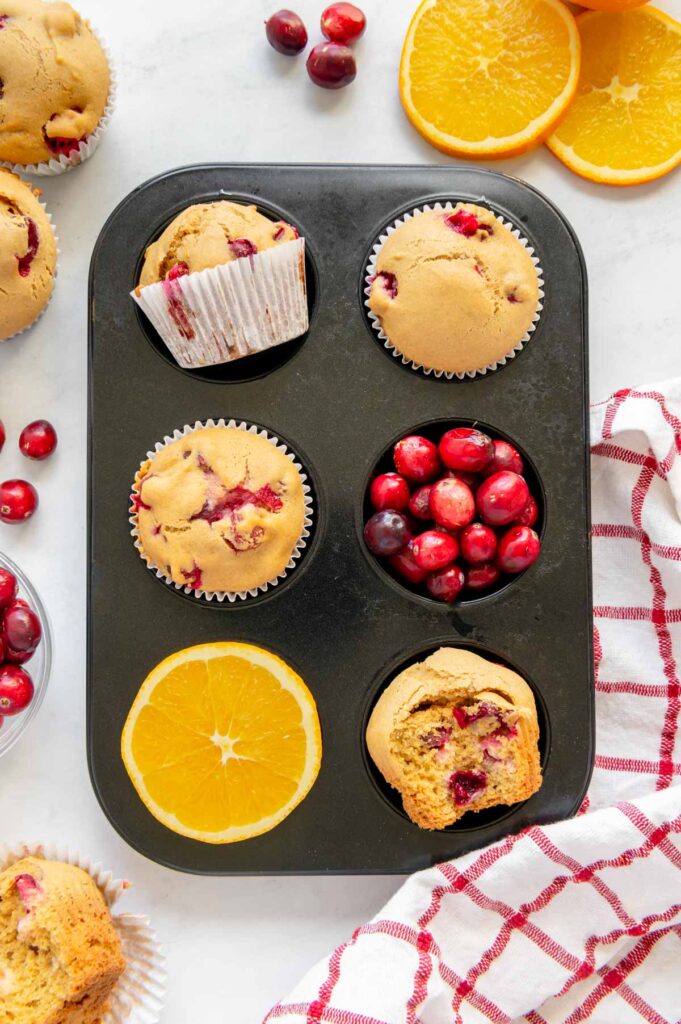 Cranberry orange muffins in a small muffin tin with fresh cranberries and orange slices.