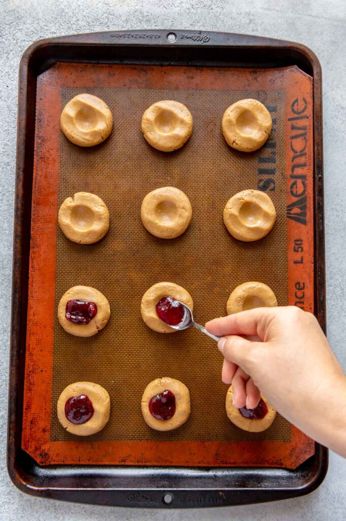 Jelly being placed in the wells of PB&J thumbprint cookies.