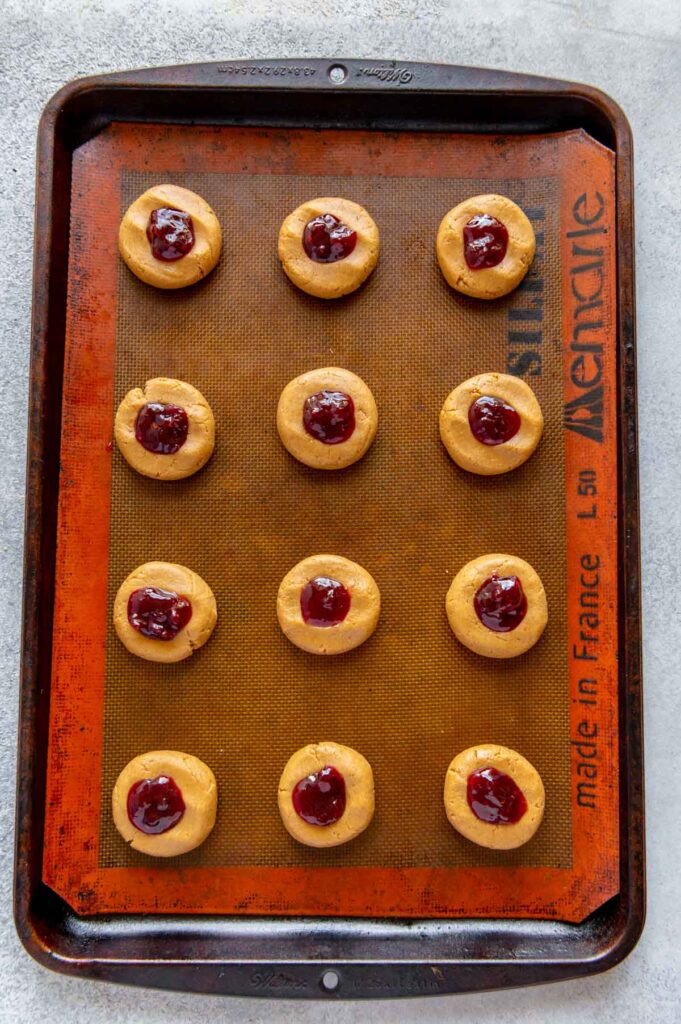 Peanut butter and jelly thumbprint cookies ready to be baked on a baking sheet.