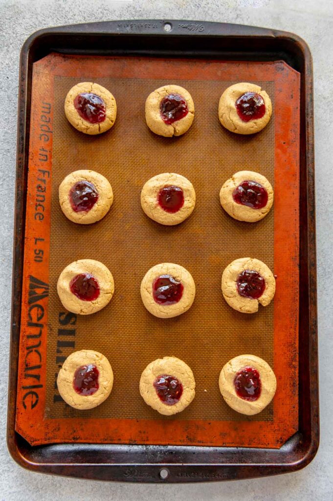 Fresh PB&J thumbpring cookies on a baking sheet pulled out of the oven.