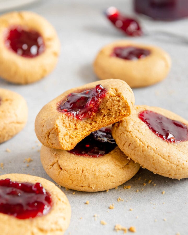 A vegan peanut butter and jelly thumbprint cookie with a bite taken out of it.