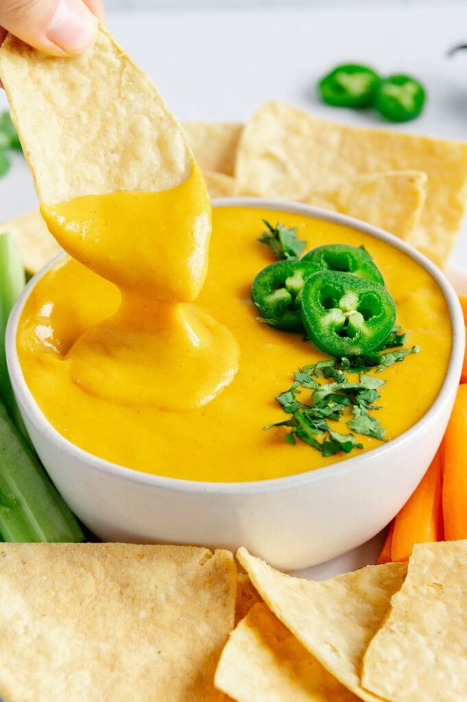 Cheesy and gooey vegan nacho cheese with a chip being dipped.