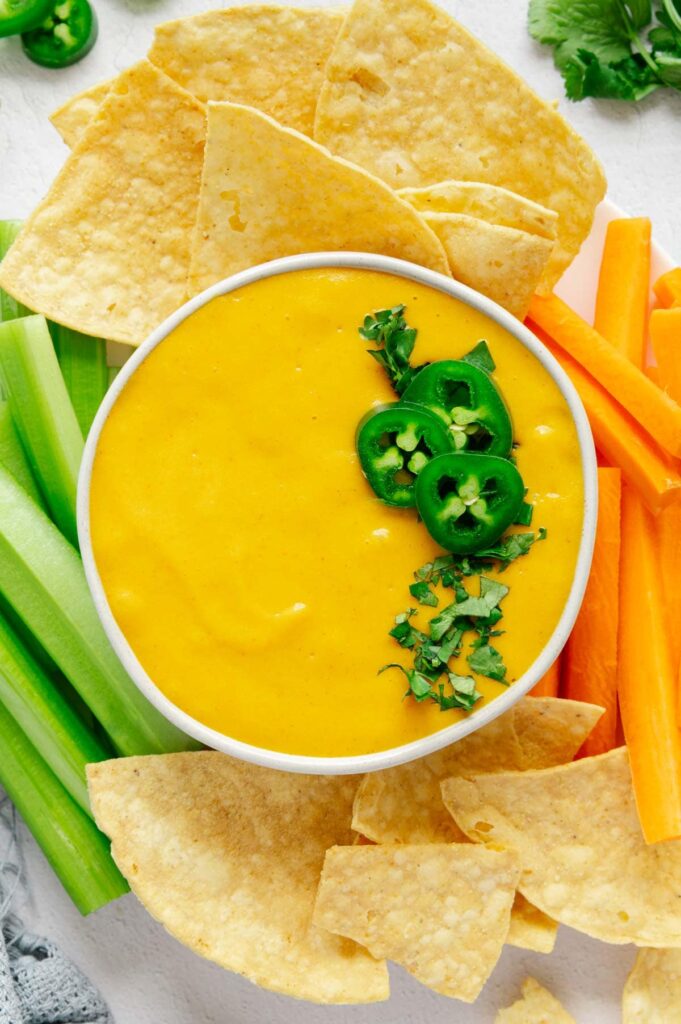 A serving platter of chips and veggies with vegan nacho cheese.