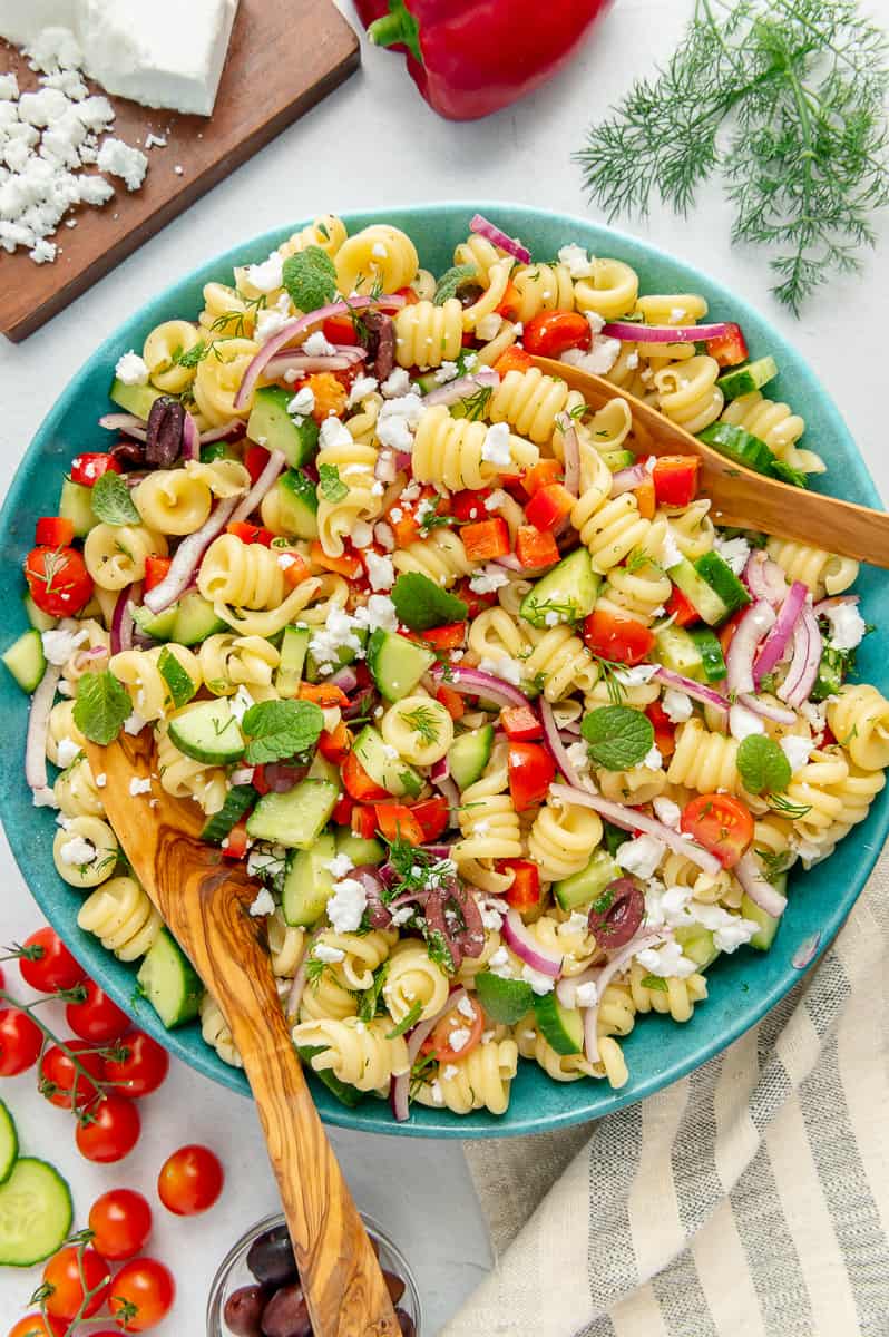 Vegan Mediterranean pasta salad in a blue serving bowl with wood serving spoons.