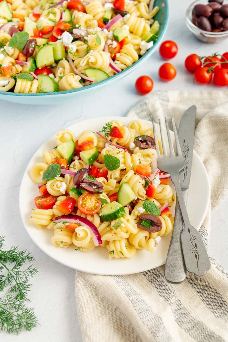 A white plate with a fork and knife on it and a serving of pasta salad.