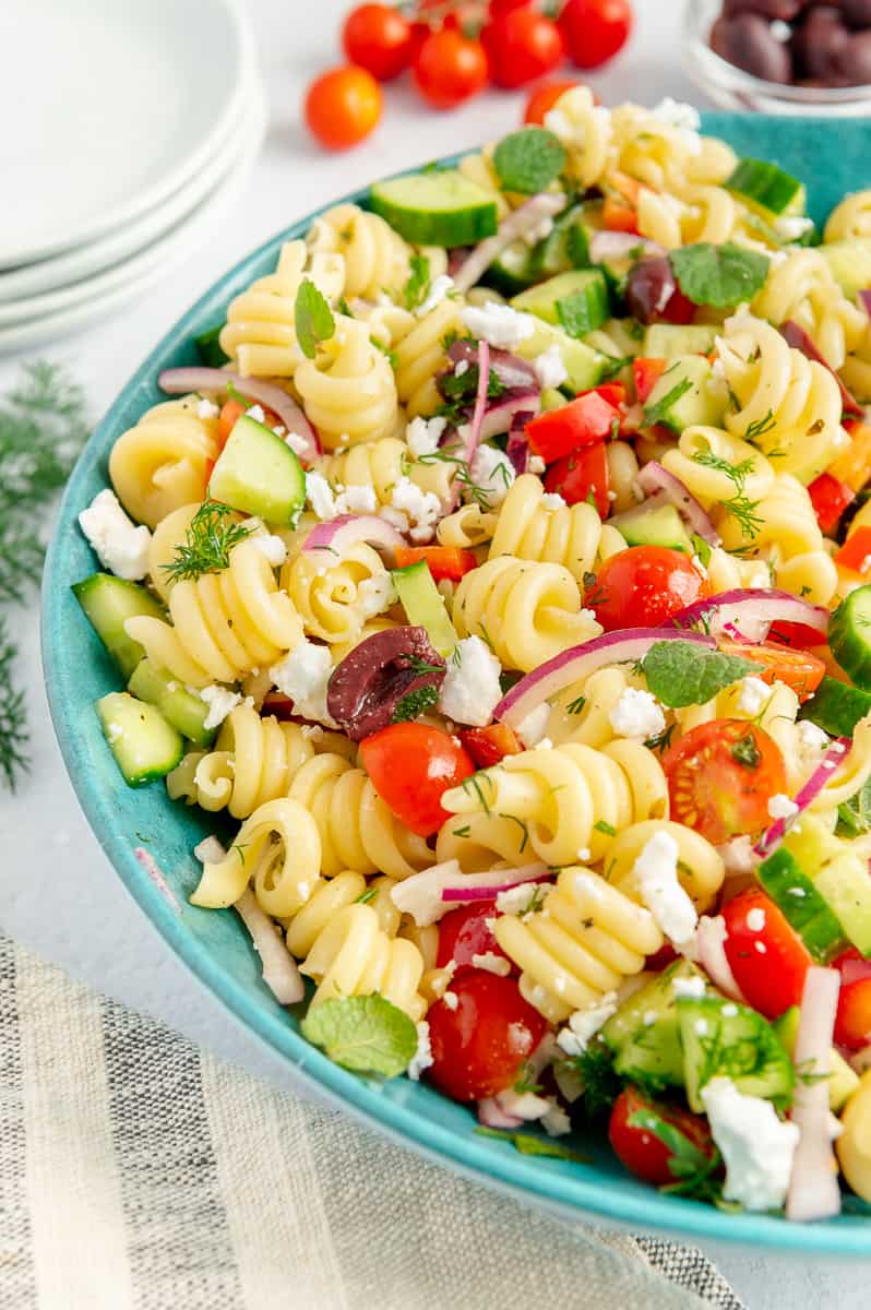 Upclose of a veggie-filled pasta salad in a blue serving bowl.