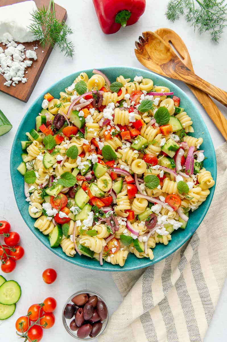 Mediterranean pasta salad garnished with fresh mint and dill in a blue serving bowl.