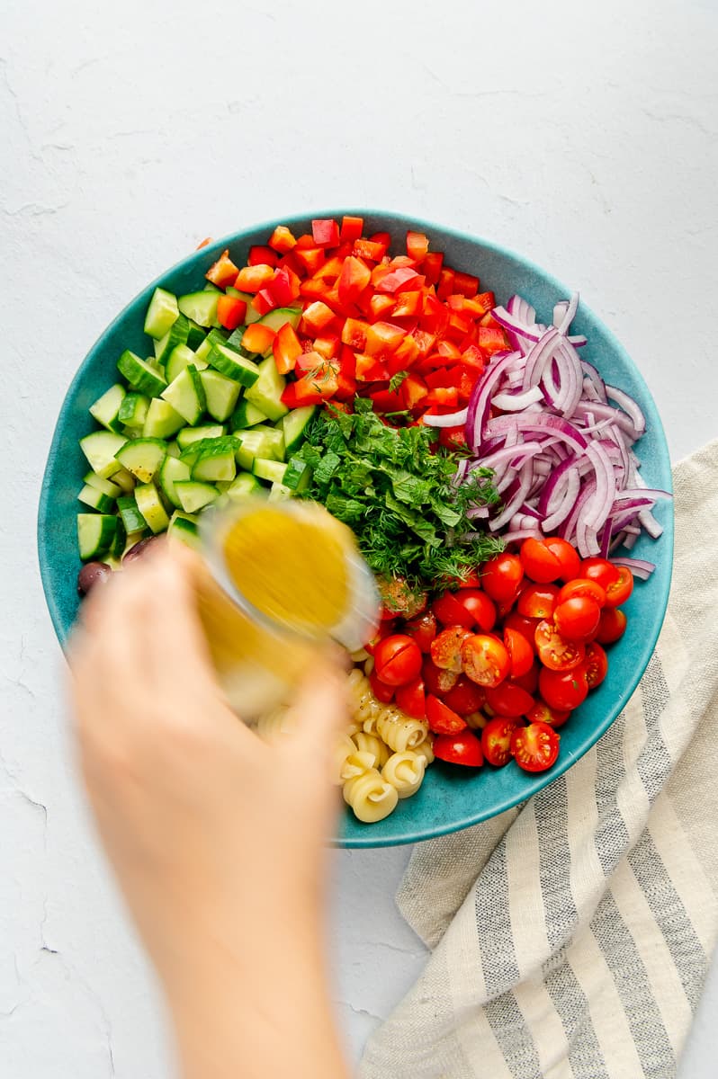 Homemade Greek dressing being drizzled over a Mediterranean pasta salad.