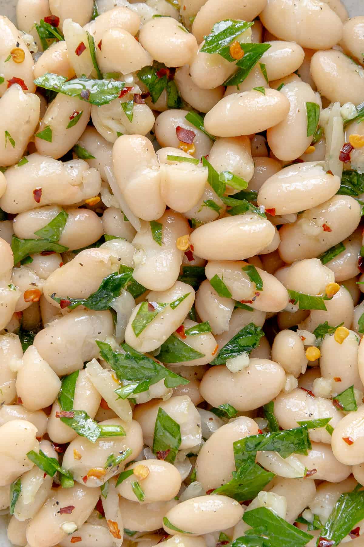 Upclose of lemon, parsley and red pepper flakes mixed with a white bean salad.
