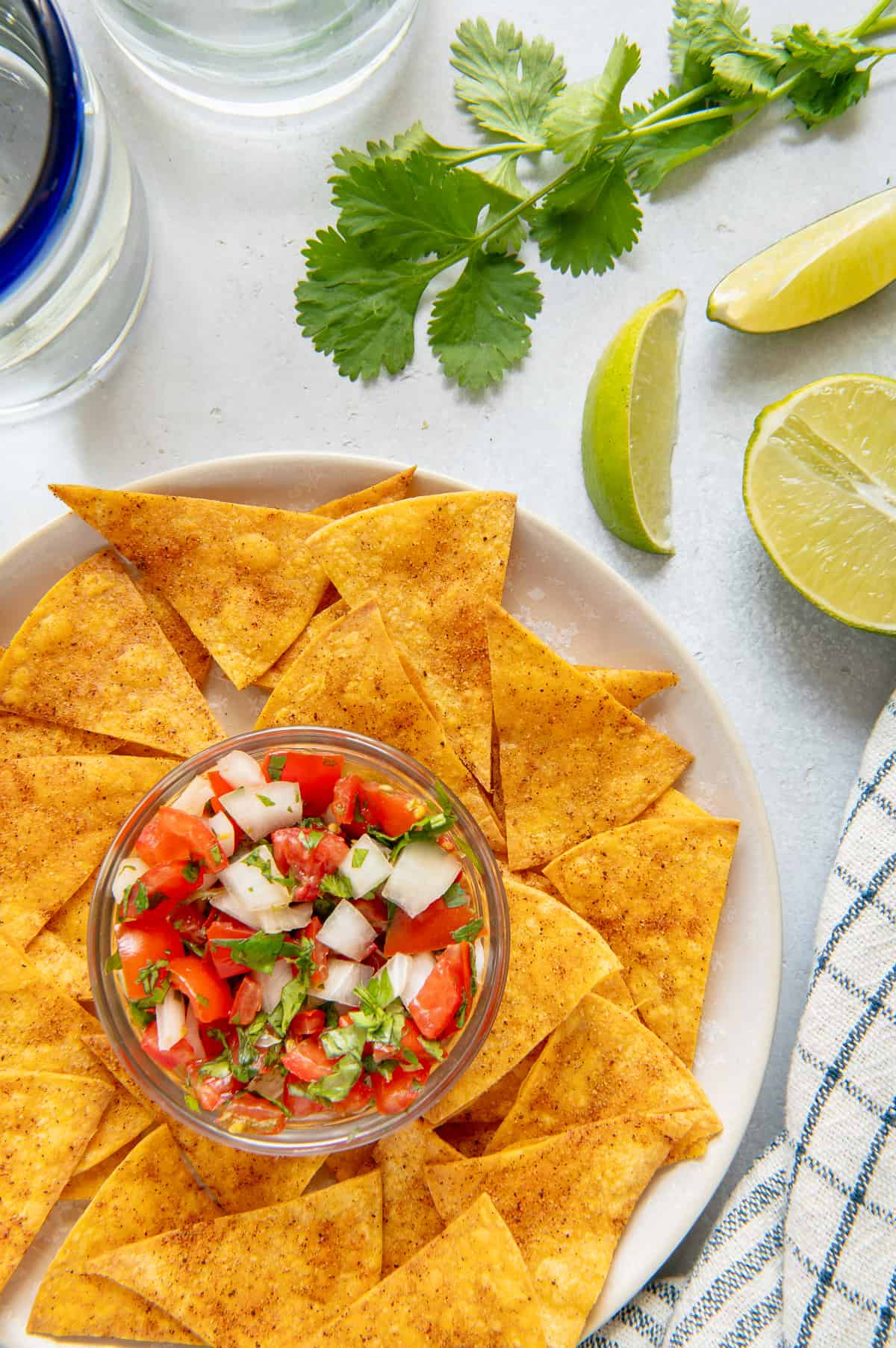 Air Fryer tortilla chips on a serving plate with pico de gallo, lime wedges and cilantro.