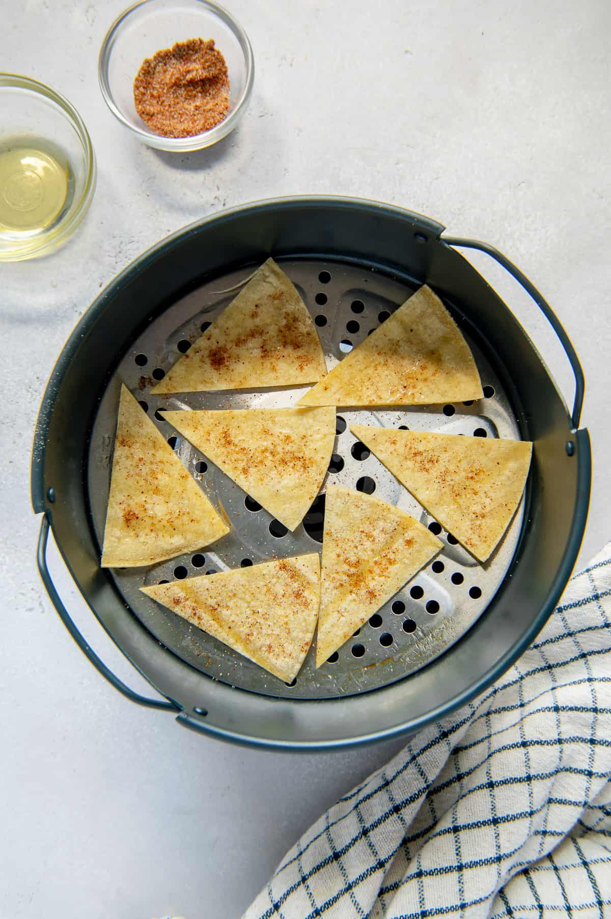 Tortilla wedges brushed with oil and sprinkled with Mexican spices in an air fryer basket.