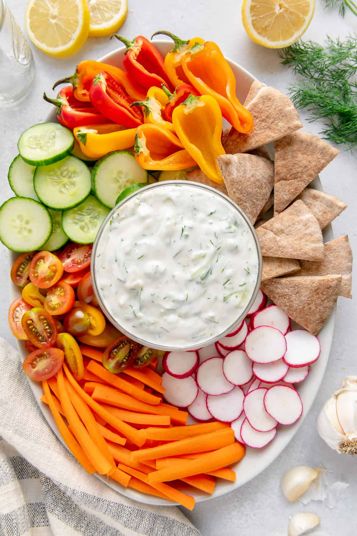 A serving platter with veggies and pita wedges served with a bowl of vegan tzatziki sauce.
