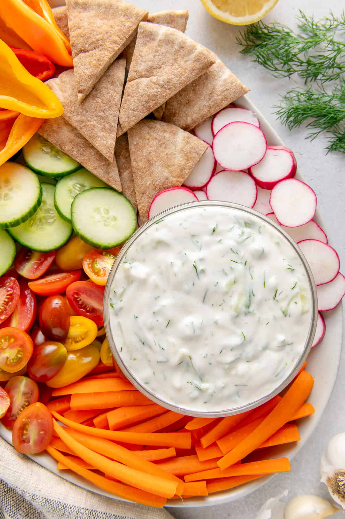 Up close of a thick and creamy 5-minute tzatziki sauce surrounded by carrots, radishes, tomatoes, cucumbers, and pita.