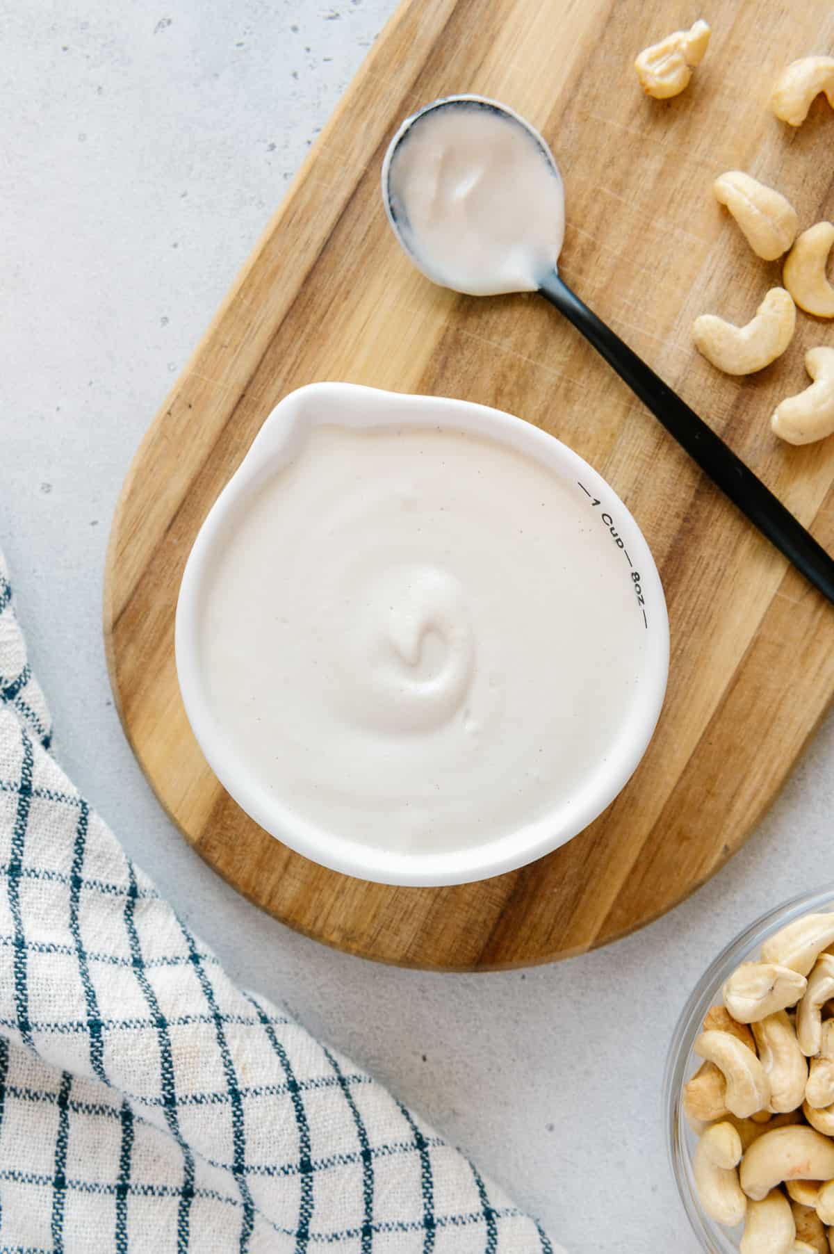 A measuring cup filled with plant-based cashew cream on a cutting board.